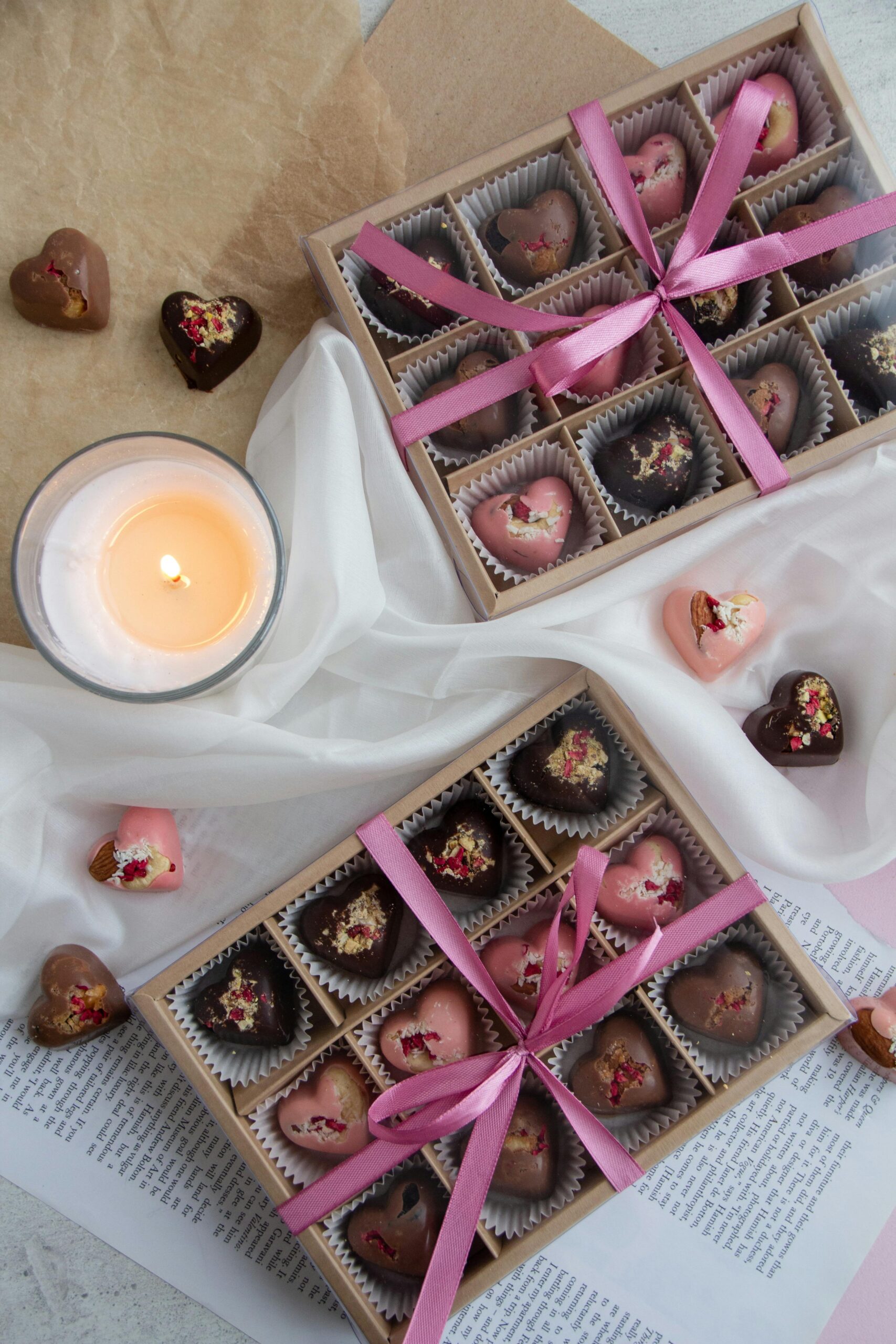 Top view of heart-shaped chocolates in gift boxes with a candle, wrapped with ribbons.