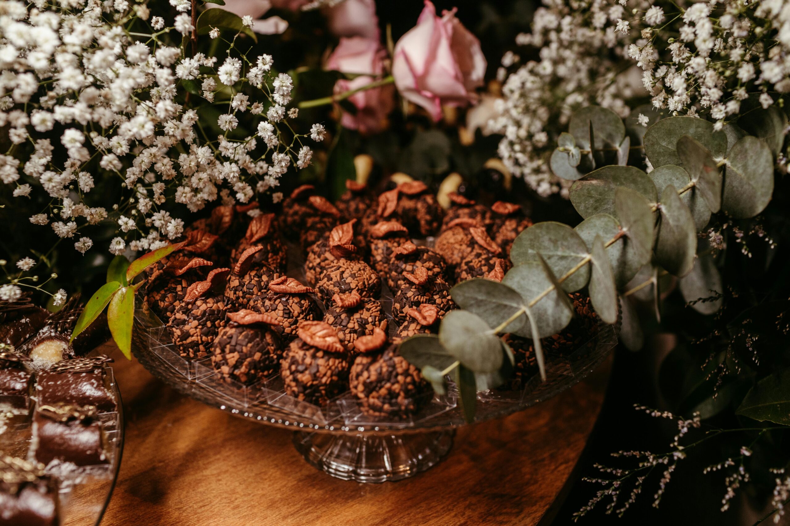 A rich display of chocolate desserts artfully arranged on a glass tray surrounded by elegant flowers.