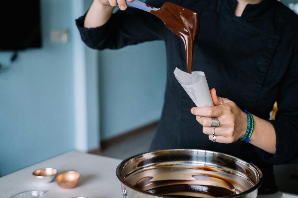 Chef pouring melted chocolate into a piping bag for food preparation in kitchen.